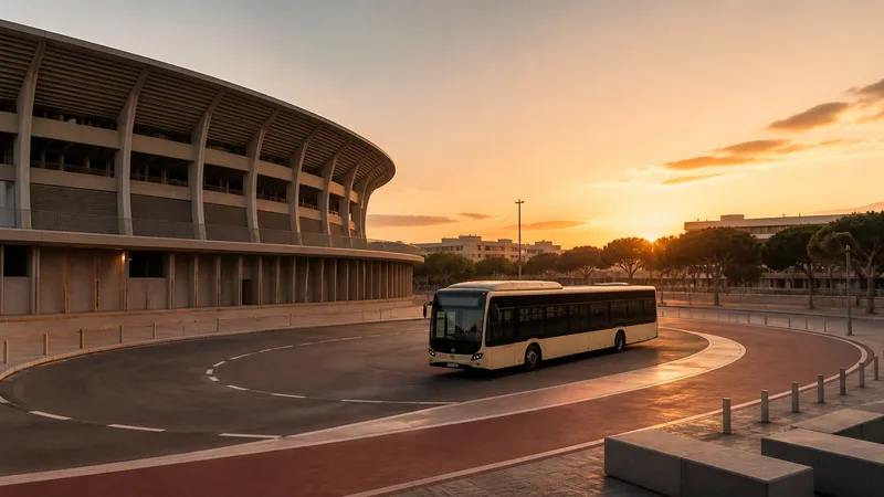 Autobús urbano sin pasajeros recorriendo un circuito señalizado alrededor de un gran estadio al atardecer