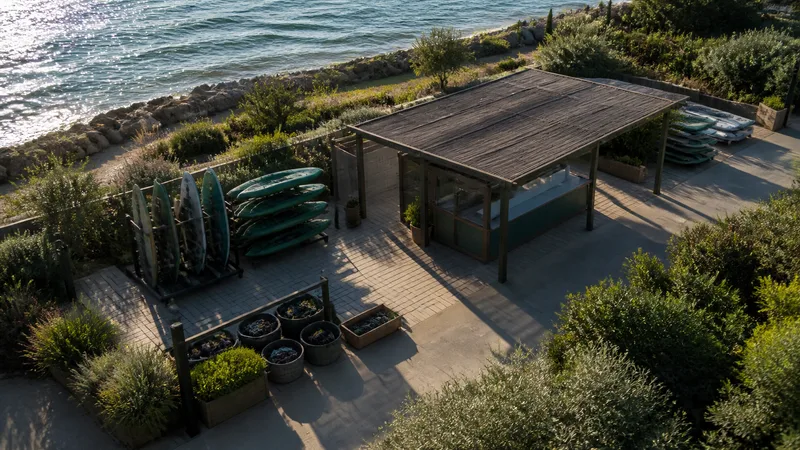Pérgola costera con un pequeño quiosco social cerrado y material de actividades marinas ordenado frente al mar