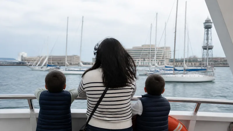 Adulto y dos niños vistos de espaldas en la cubierta de un barco de paseo frente a Barcelona