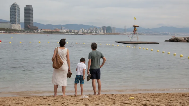 Familia vista de espaldas junto al agua en una playa urbana de Barcelona con puesto de socorro al fondo