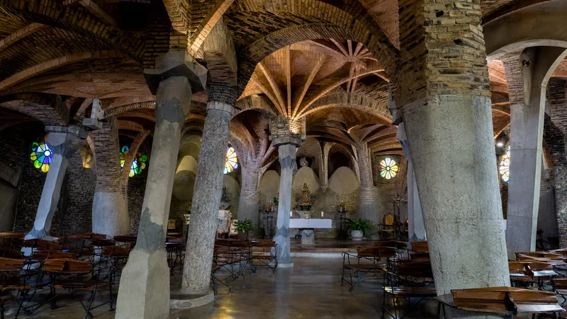 Interior de la Cripta Gaudí con columnas inclinadas, arcos de ladrillo, vitrales y bancos