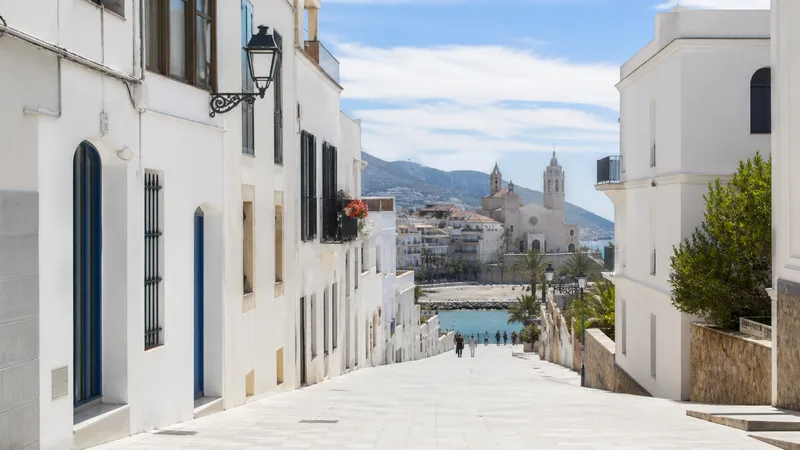 Calle peatonal blanca de Sitges descendiendo hacia el casco histórico y el mar