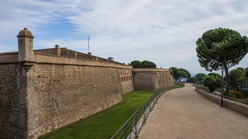 Murallas, foso verde y camino exterior del Castillo de Montjuïc entre pinos mediterráneos