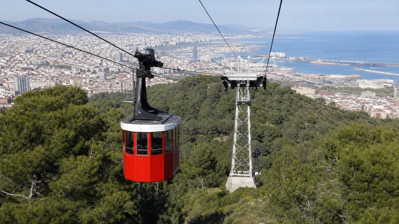 Cabina roja del Teleférico de Montjuïc sobre la ladera, con el puerto y Barcelona al fondo