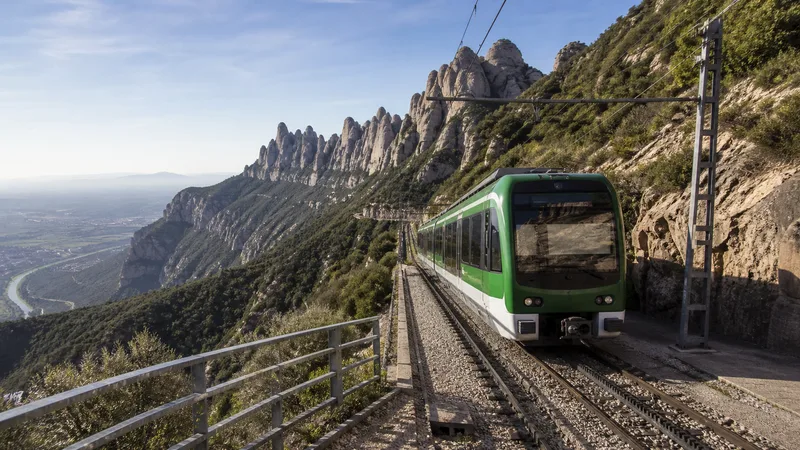 Tren cremallera verde y blanco ascendiendo por la ladera de Montserrat con el valle al fondo