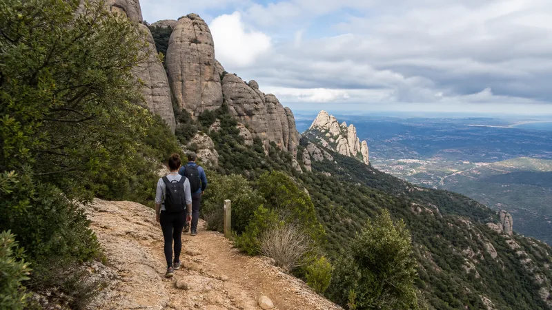Dos excursionistas de espaldas por un sendero señalizado entre agujas y vegetación de Montserrat