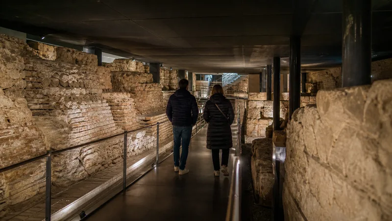 Visitantes recorriendo por una pasarela restos arqueológicos romanos bajo Barcelona