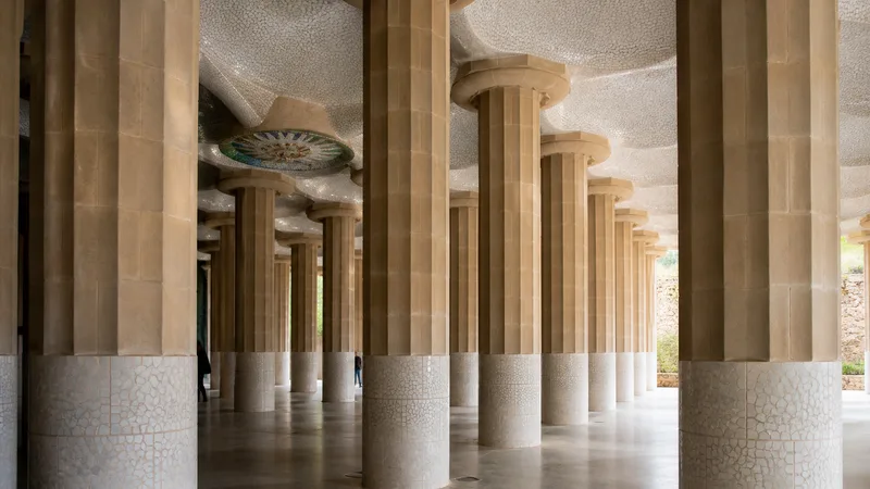 Interior de la sala hipóstila del Park Güell, con columnas de piedra, techo de mosaico y luz natural