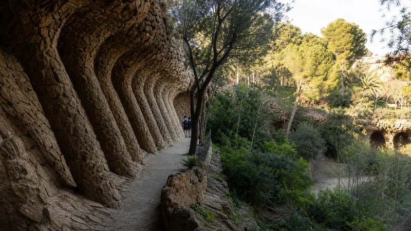 Camino en pendiente bajo un viaducto de piedra del Park Güell, integrado en vegetación mediterránea