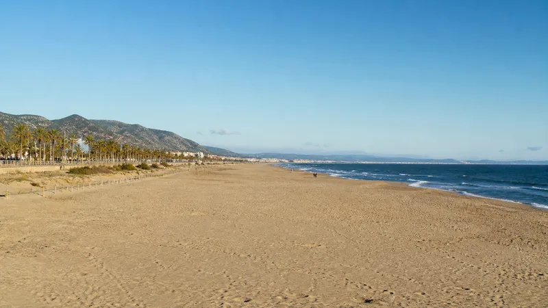 Arenal ancho y largo de Castelldefels con dunas bajas y relieve litoral al fondo