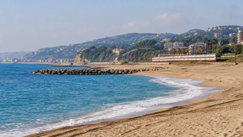 Tren circulando junto a una playa del Maresme con espigones y colinas costeras