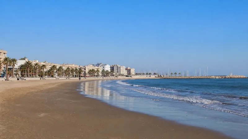 Arenal de Vilanova i la Geltrú con paseo, edificios bajos, puerto y espigón