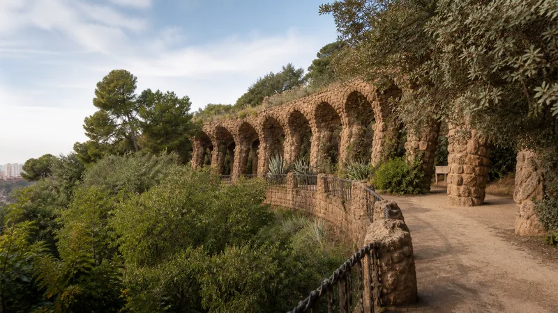 Viaducto de piedra y sendero entre vegetación mediterránea en el Park Güell