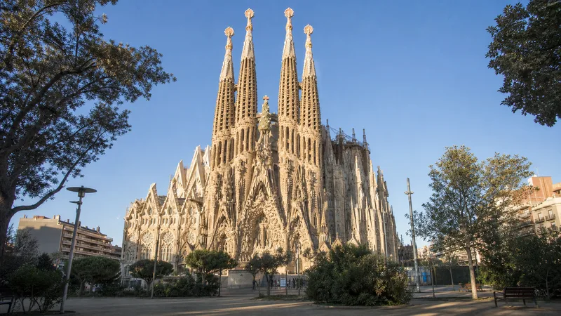 Sagrada Família vista desde una plaza arbolada de Barcelona a primera hora de la mañana