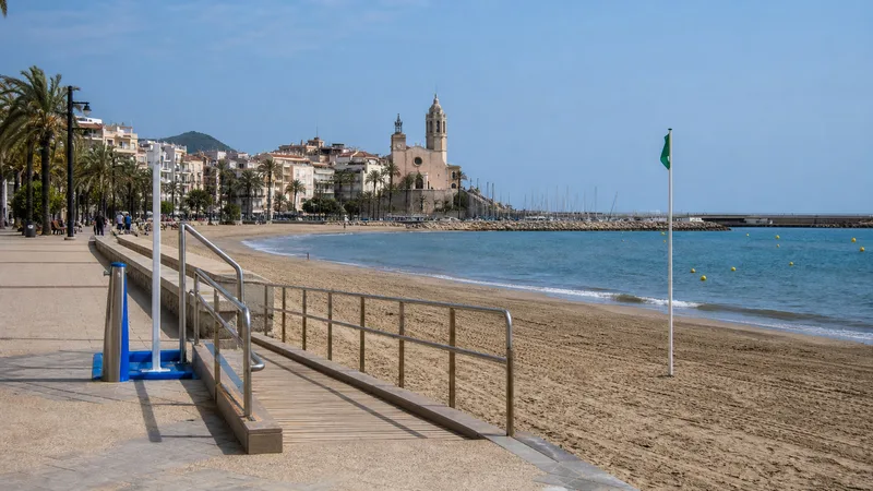 Playa urbana de Sitges con paseo marítimo, pasarela accesible y el frente histórico al fondo